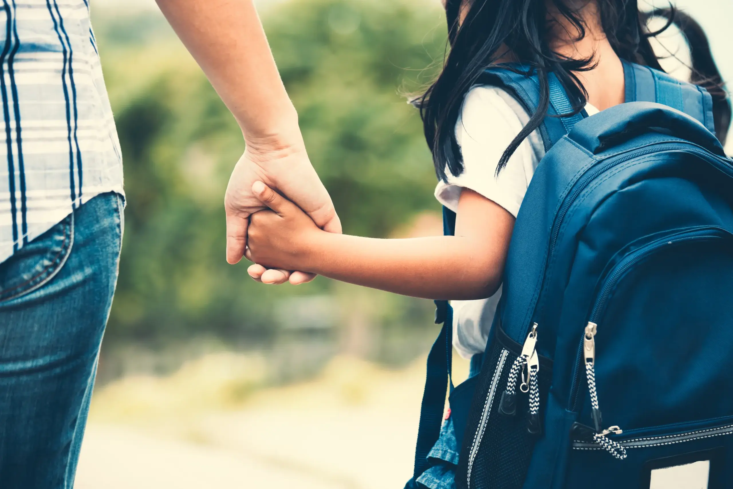 A mother holding the child's hand walking to school.