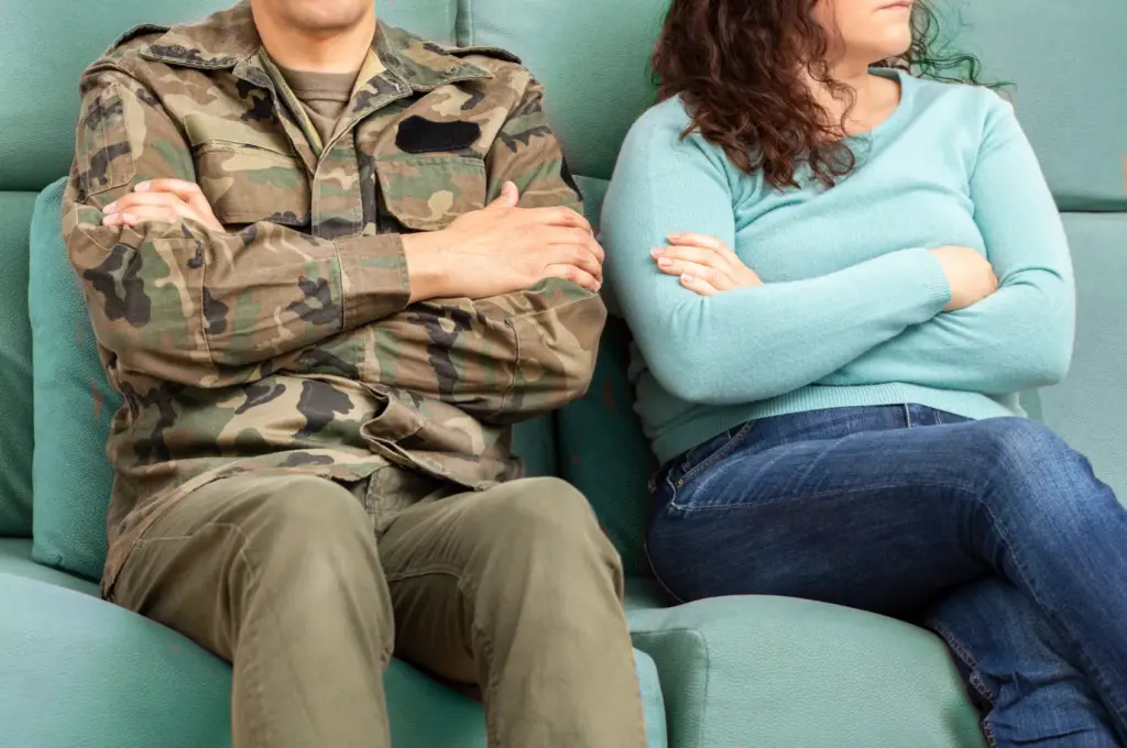 A military service member with his wife sitting on a couch with arms crossed.